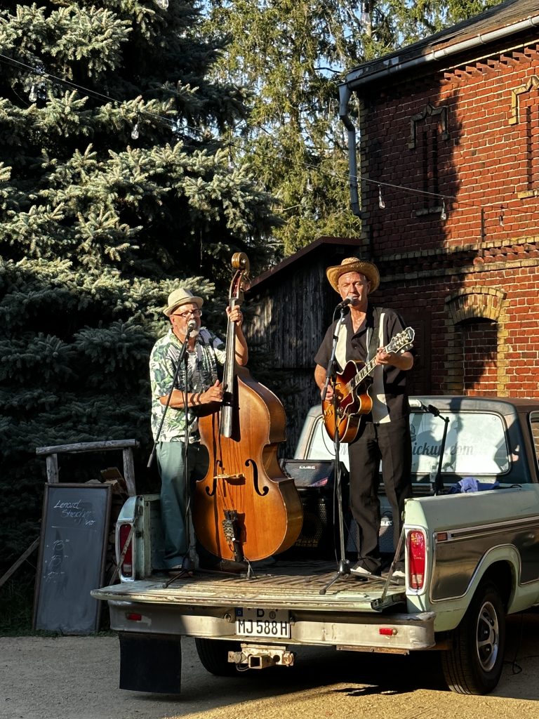Junge Musiker auf einem mobilen Bühnenwagen spielen akustische Gitarre und Kontrabass im Garten.