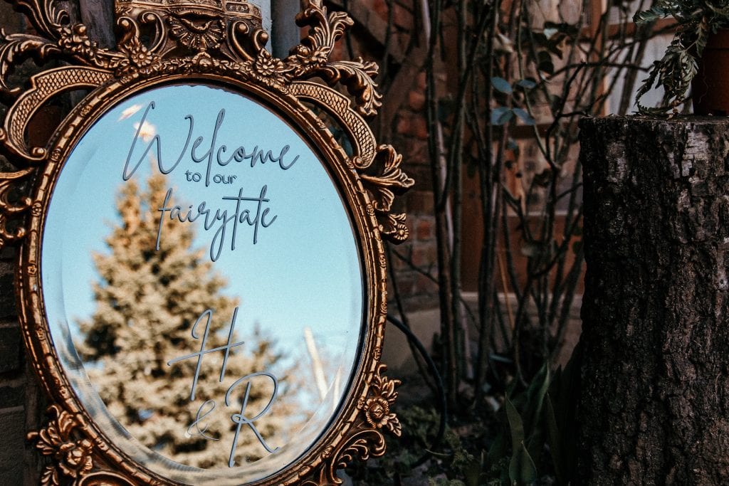 Einladender Spiegel mit Goldrahmen, der den Schriftzug „Welcome to our fairytale Home & R“ reflektiert, umgeben vonNatur und Vintage-Charme.