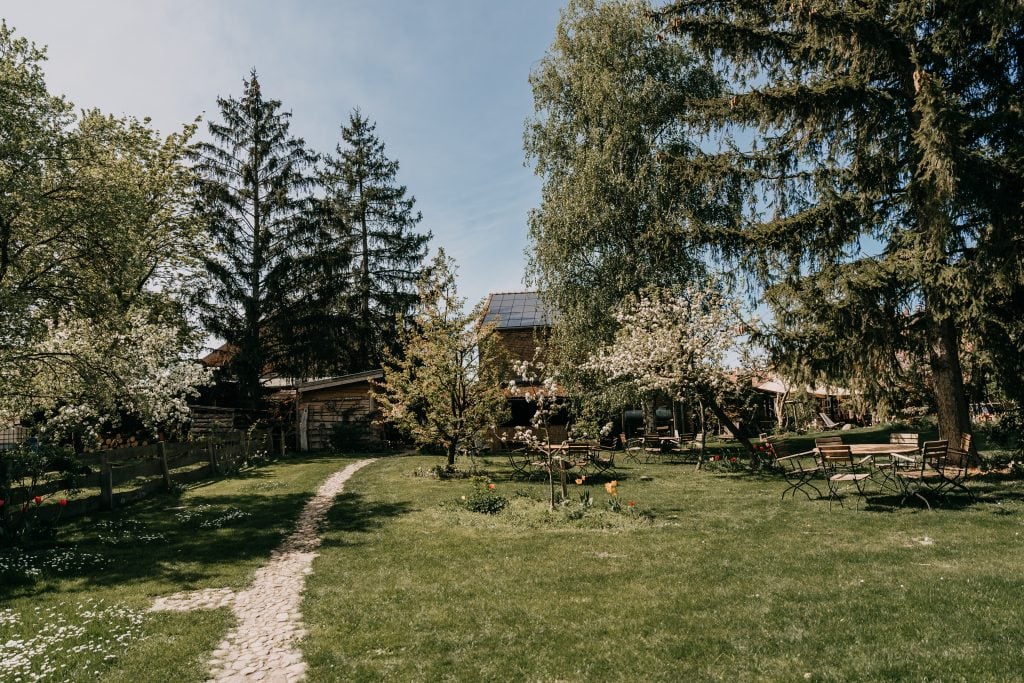 Entspannter Garten mit blühenden Bäumen, Sitzgelegenheiten und Solardach im Grünen.