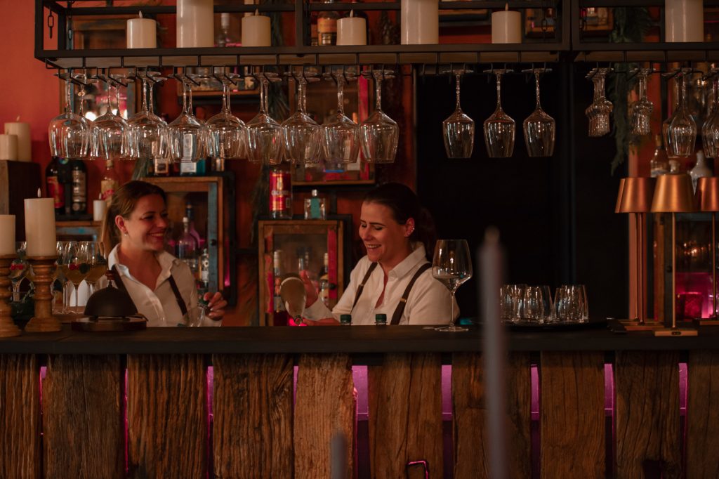 Entspannte Bar-Szene mit zwei Frauen, die lachen und Getränke genießen, stilvoller Ambiente, gemütliche Atmosphäre.