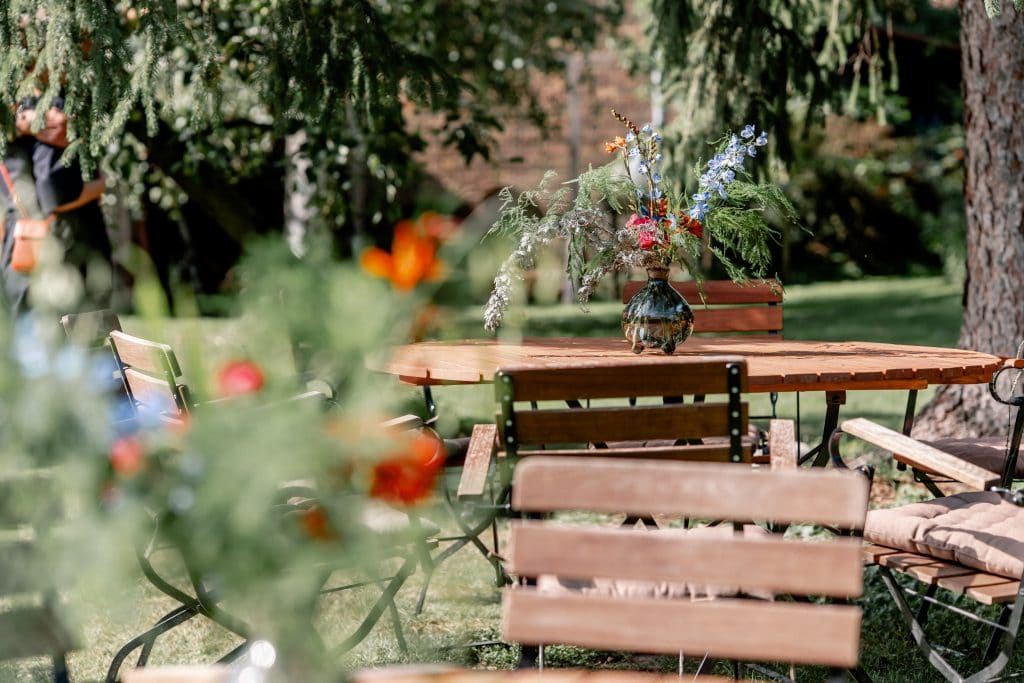 1. Gem&uuml;tlicher Garten mit Holztisch und Blumenvasen im Gr&uuml;nen, ideal f&uuml;r entspannte Momente.