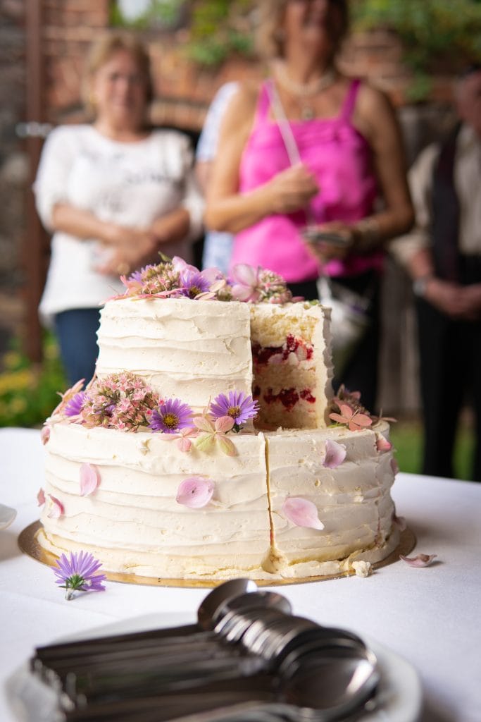 Kundinnen schneiden beim Sommerfest einen Hochzeitstorte mit Blumenverzierung.