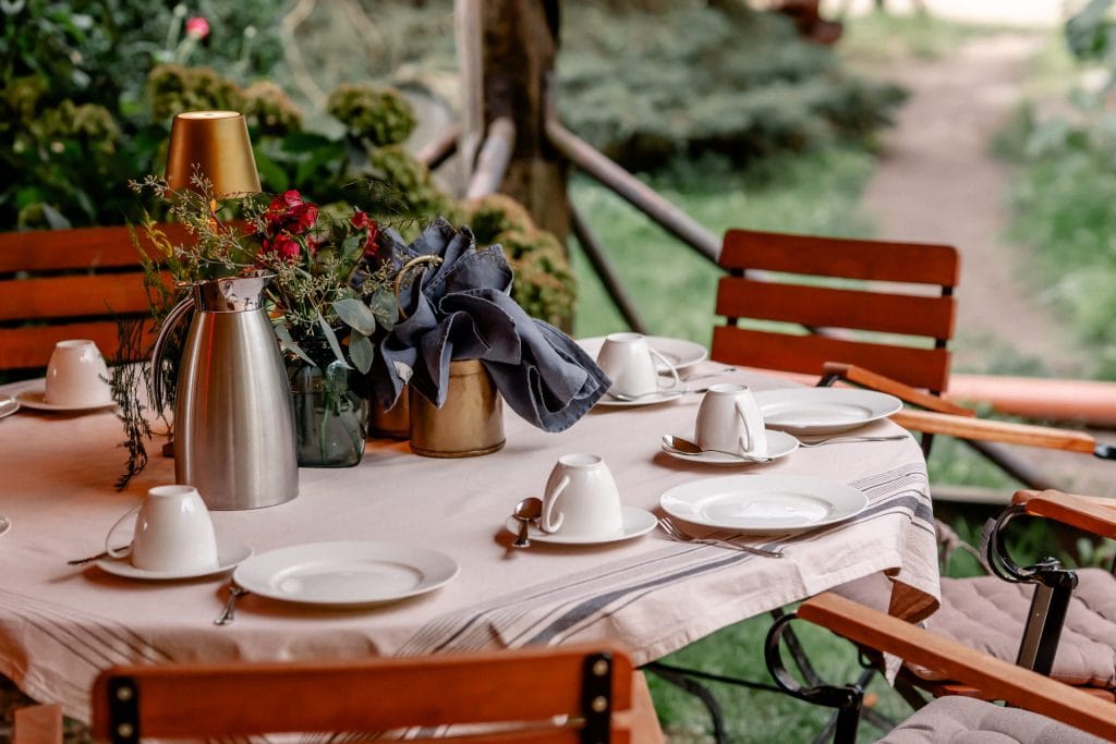 Gem&uuml;tlicher Gartentisch mit Blumen, Geschirr und Besteck auf der Terrasse im Gr&uuml;nen.
