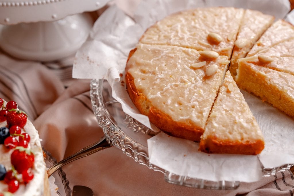 Saftiger Zitronenkuchen mit Mandeln auf Glasplatte, glutenfrei, vegane Bäckerei, glutenarme Backwaren, gesunde Kuchenoptionen.