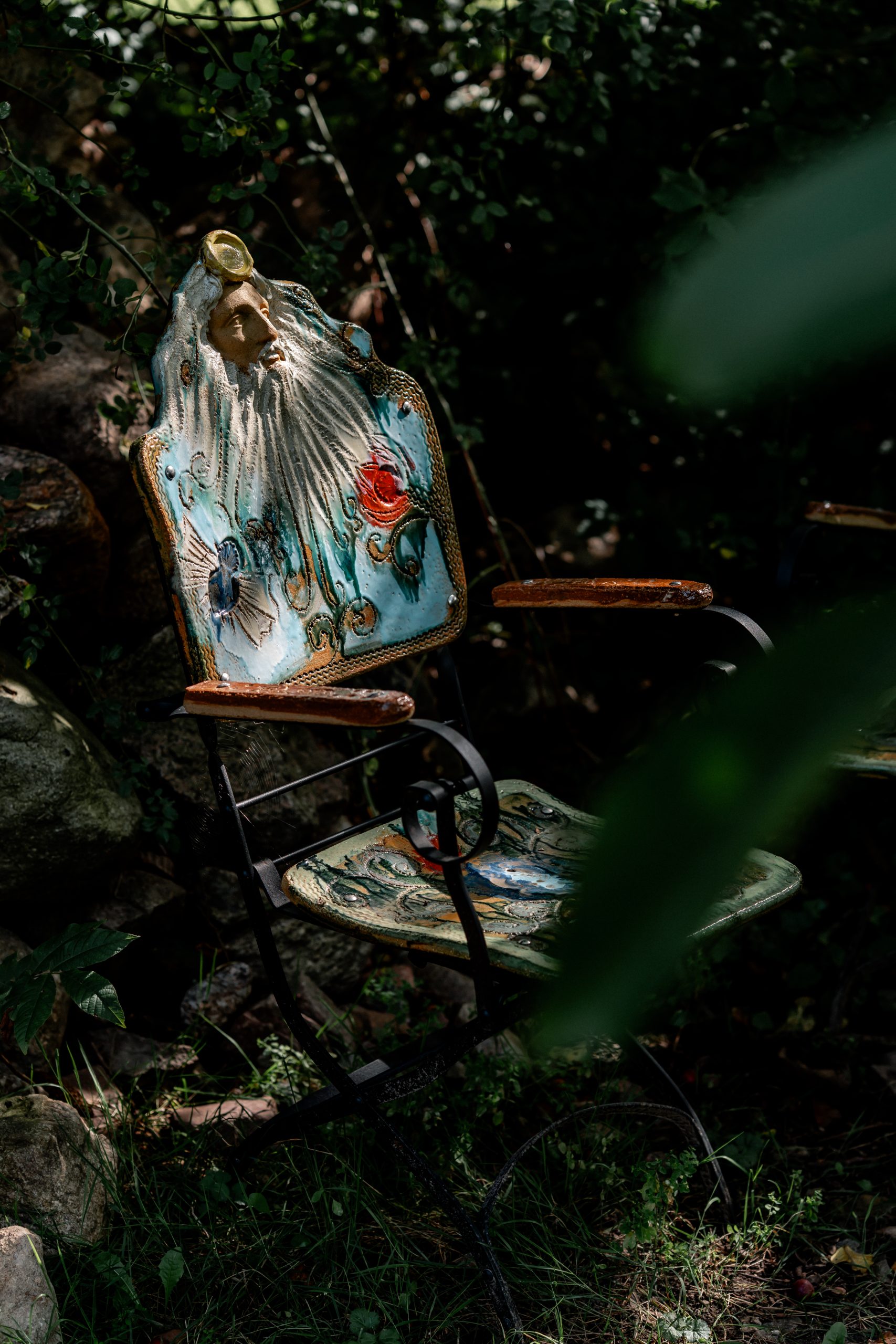 Farbige Gdrn mit religiösem Motiv, Gartenbank, Garten, Natur, antike Gartendekoration, Kunst im Garten, entspannte Atmosphäre.