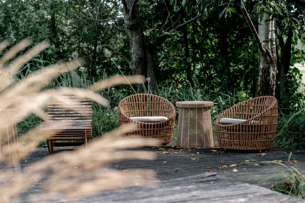 Gemütlicher Außenbereich mit Rattanmöbeln und Naturgarten im nachhaltigen Lebensstil.