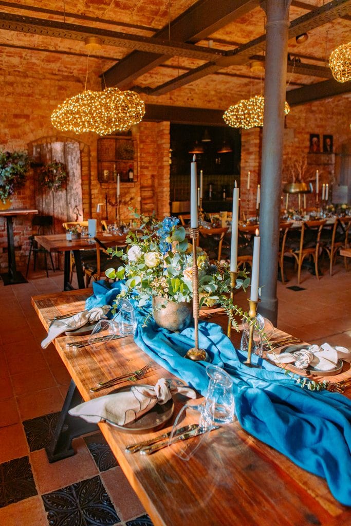 1. Elegante festliche Tafel mit Blumen, Kerzen und blauer Tischdekoration in rustikalem Ambiente.