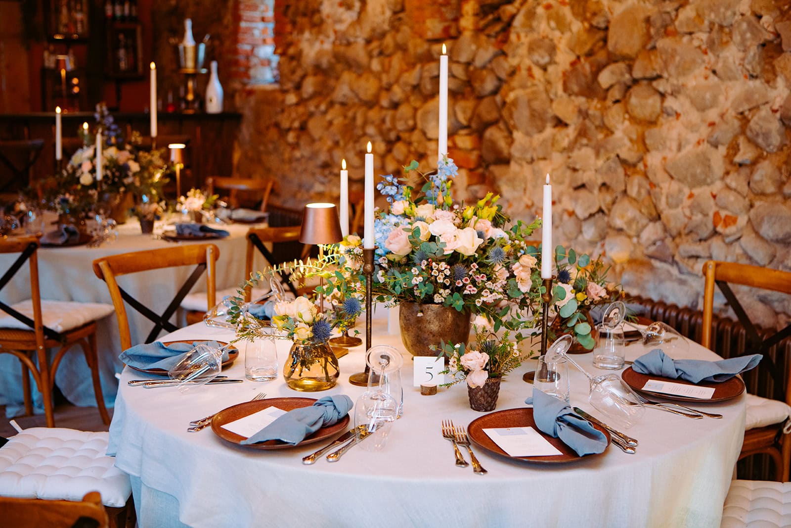 Blumenarrangement und Kerzen auf weißem Geschirr für Hochzeitsfeier bei Gut Leben Berlin.