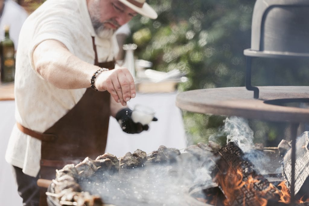 Arbeit an authentischem Holzgrill beim Outdoor-Koch-Event, Fokus auf nachhaltiges Grillen und Frische.