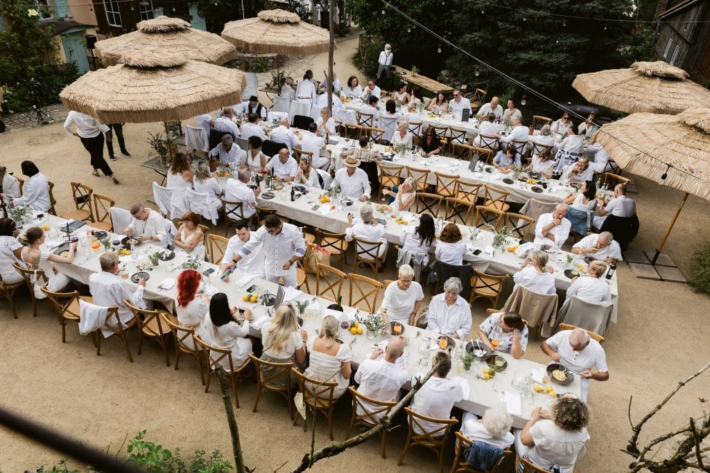 Fröhliche Menschen beim gemeinsamen Essen im Garten mit Sonnenschirmen, perfektes Sommerfest.
