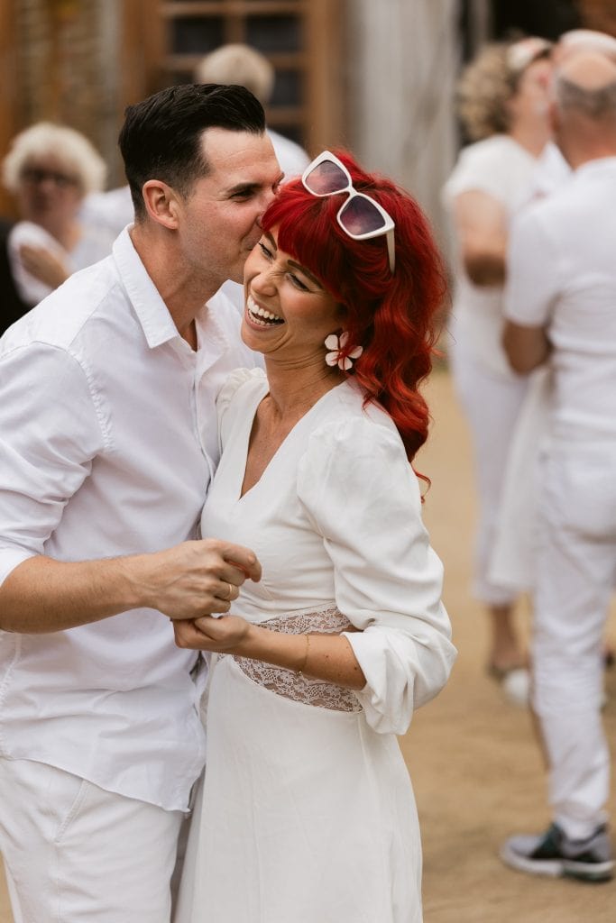 Fr&ouml;hliches Paar bei der Feier im Stil von Gut Leben Berlin, entspanntes Gemeinschaftserlebnis in wei&szlig;em Outfit.