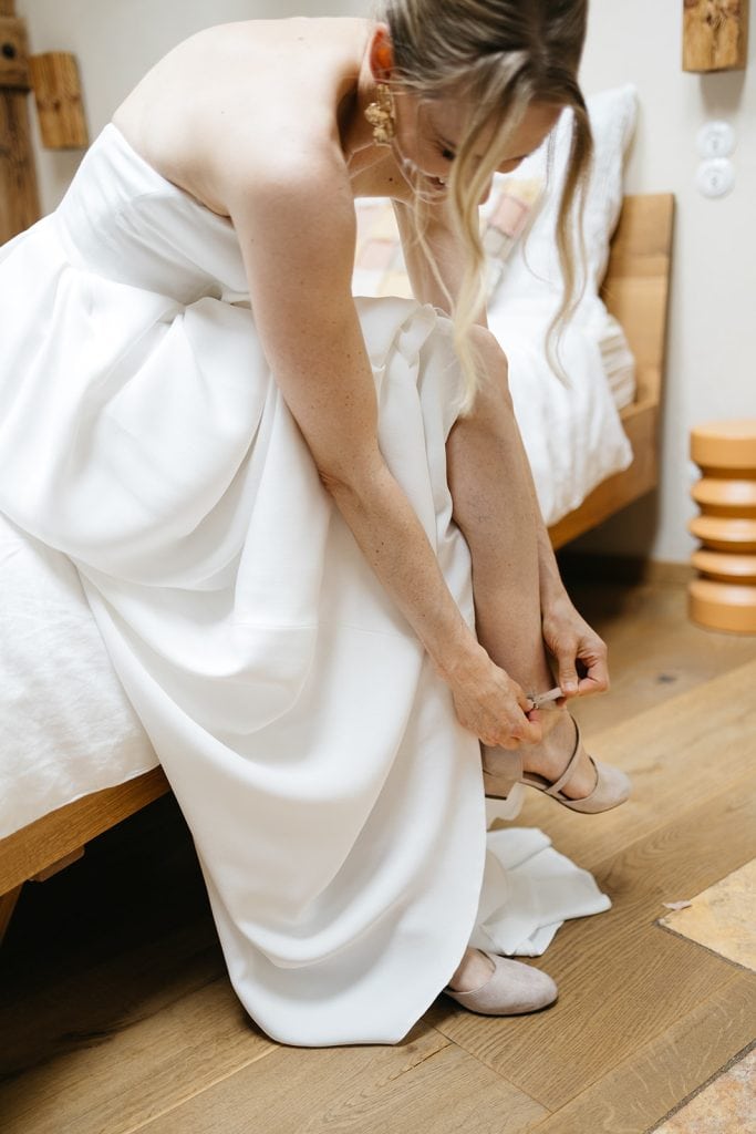 Elegante Braut zieht Schuhe an, gemütliche Atmosphäre, Hochzeitsvorbereitungen, natürlicher Stil.