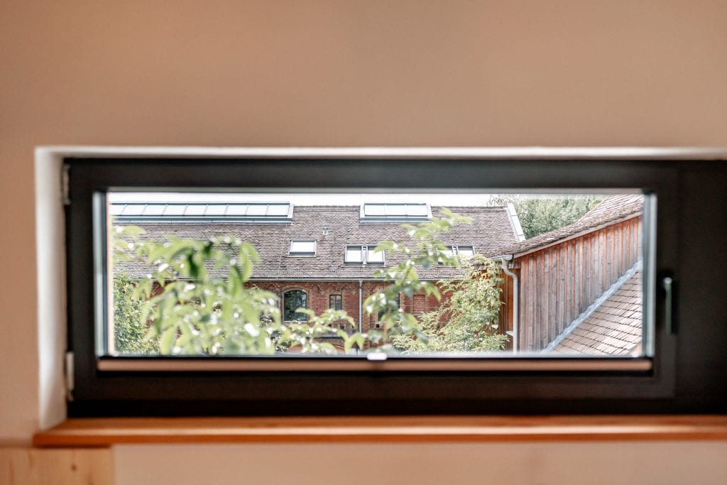Blick durch ein Fenster auf ein historichem Geb&auml;ude mit Dachfenstern und B&auml;umen in Berlin.