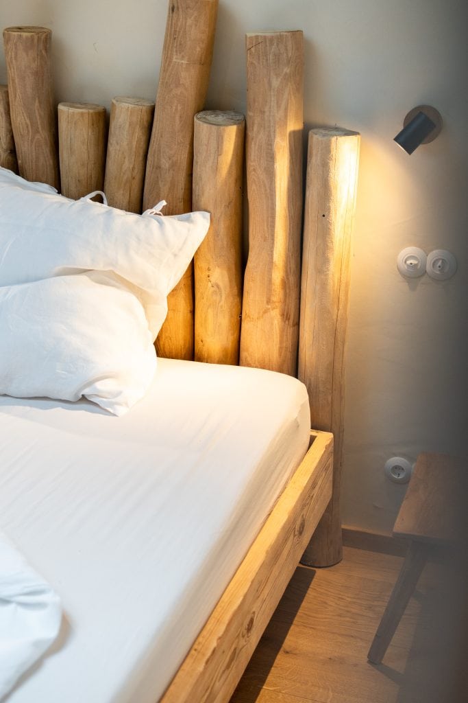 Naturholzbett mit stilvollem Kopfteil aus Baumstämmen, gemütliches Schlafzimmer, nachhaltiges Wohndesign.