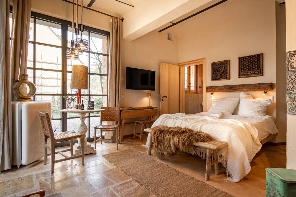 Gem&uuml;tliches Schlafzimmer mit Naturholzm&ouml;beln, viel Tageslicht und rustikalem Dekor f&uuml;r nachhaltigen Wellnessurlaub.