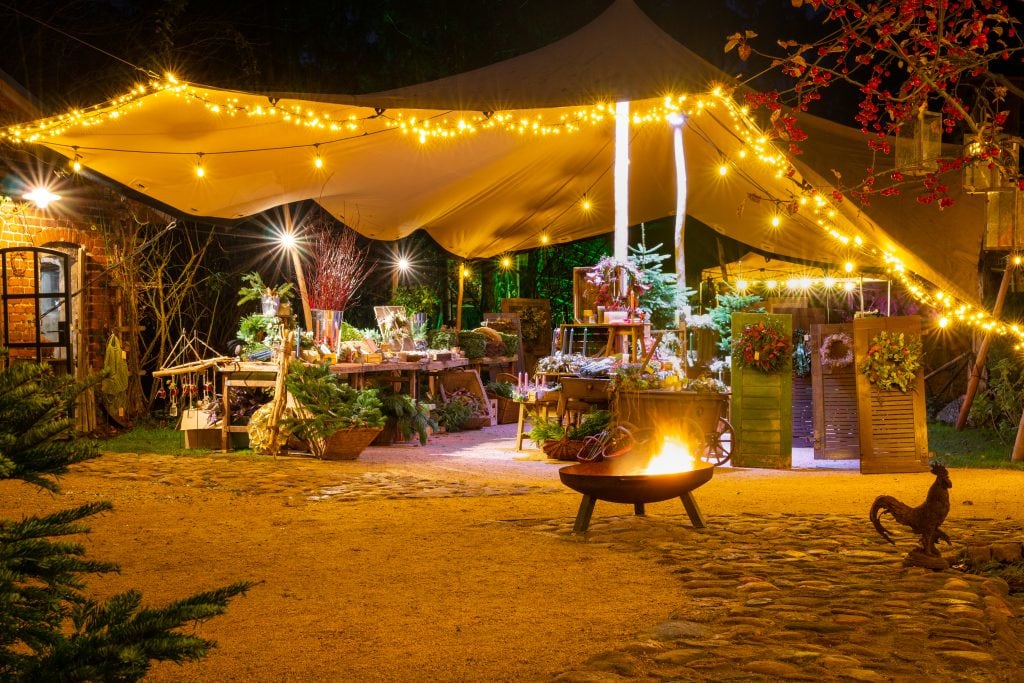 Gemütlicher Outdoor-Weihnachtsmarkt mit Lichterketten, festlicher Dekoration und Feuerplatz in Berlin.