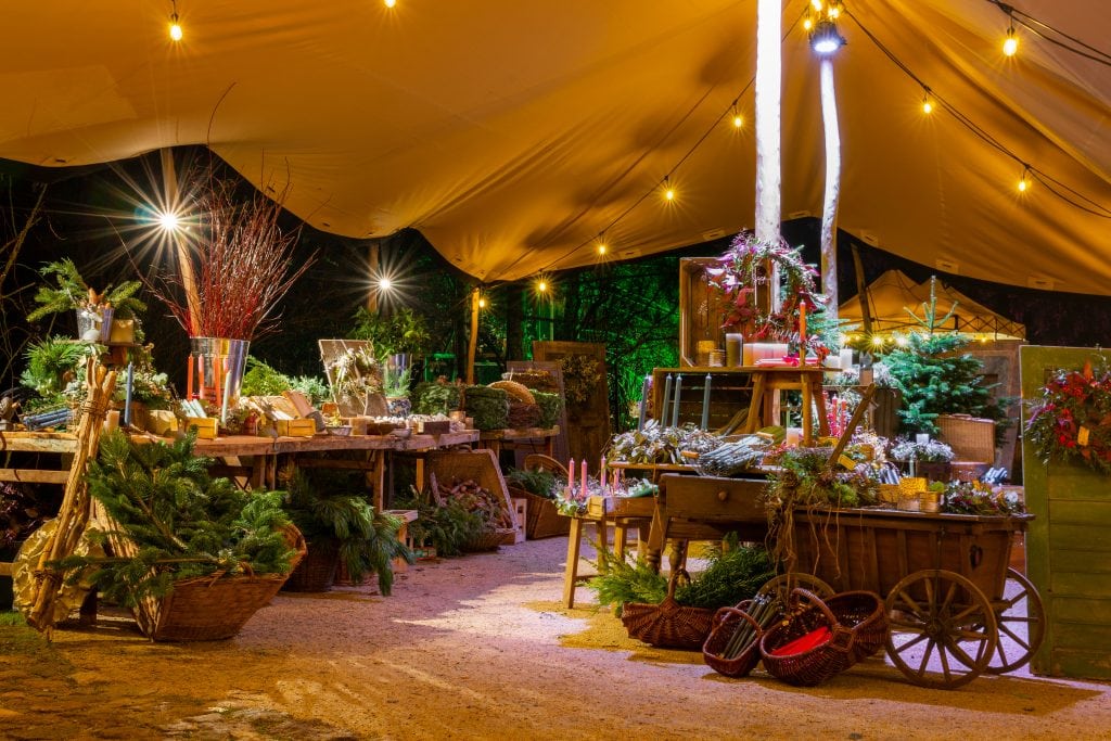Optischer Blick auf einen festlich geschmückten Weihnachtsmarktstand mit Dekorationen und Lichterketten im Nachtlicht.