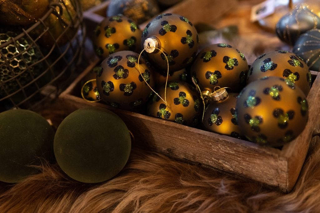 Gl&auml;nzende goldene Weihnachtskugeln mit schwarzen und gr&uuml;nen Mustern in einer rustikalen Holzschachtel.