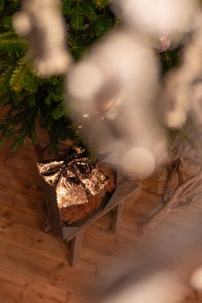 Festlich geschm&uuml;ckter Weihnachtsbaum mit Glanzdekoration und Geschenk auf Holzbank, besinnliche Atmosph&auml;re.