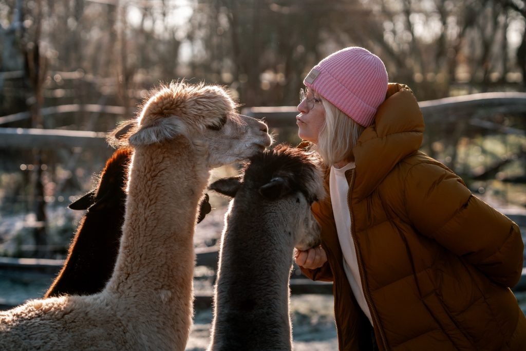 Fröhliche Frau mit Almata und Lamas in der Natur, entspannt und glücklich, Naturerlebnis, Tierliebe, Auszeit in der Natur.