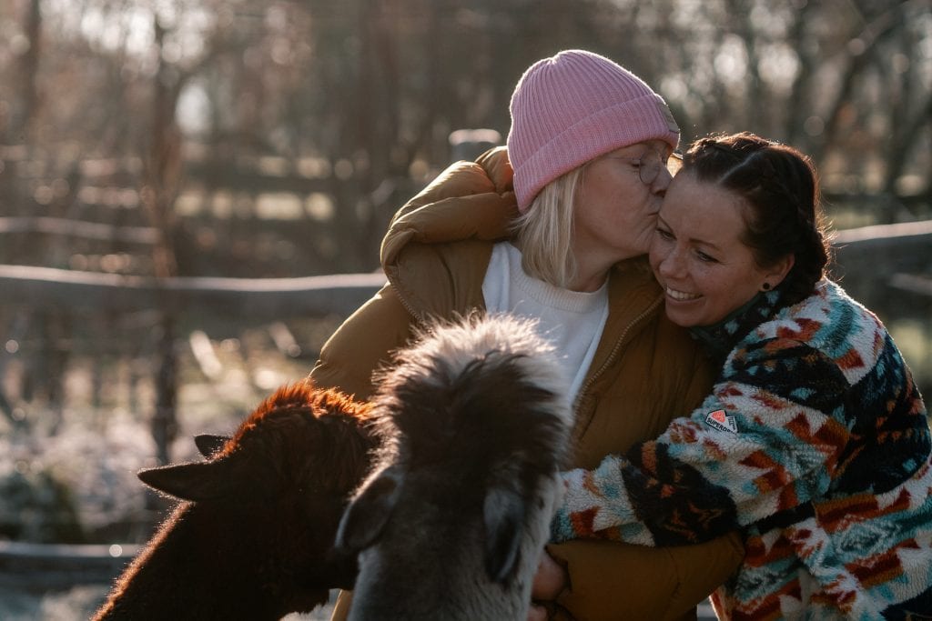 Fr&ouml;hliche Frauen k&uuml;ssen sich im Wald, mit Tieren und Natur, Fokus auf Wohlbefinden und Nachhaltigkeit.