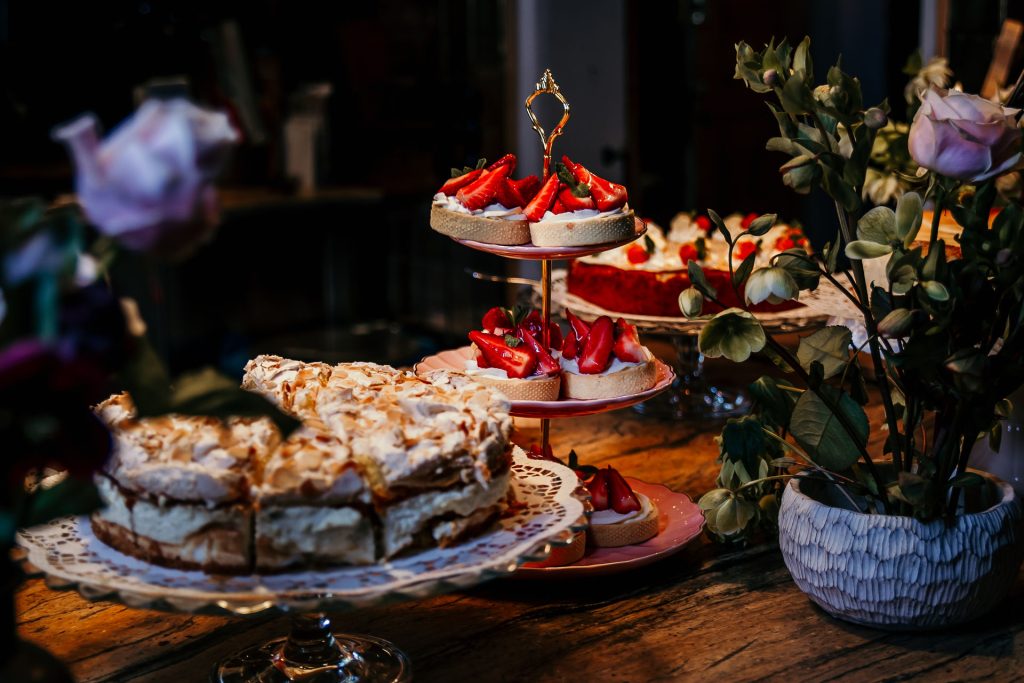 Frische Erdbeert&ouml;rtchen und Torten auf einem stilvollen Kuchenteller mit Blumenarrangement.