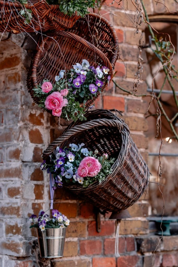 Fr&uuml;hlingsblumen in Korbgef&auml;&szlig;en an Ziegelmauer, naturverbundenes G&auml;rtnern, Gartenstil, Gartendekoration, Blumenarrangement.