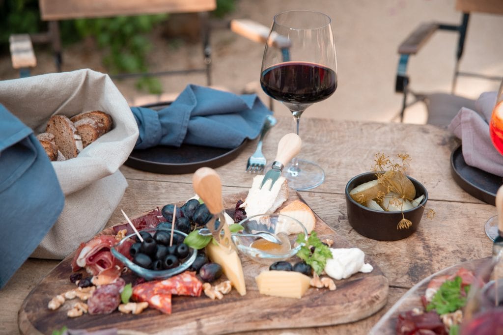 Fr&uuml;hst&uuml;ck mit K&auml;se, Wurst, Wein und Oliven auf einem rustikalen Holztisch im Garten.
