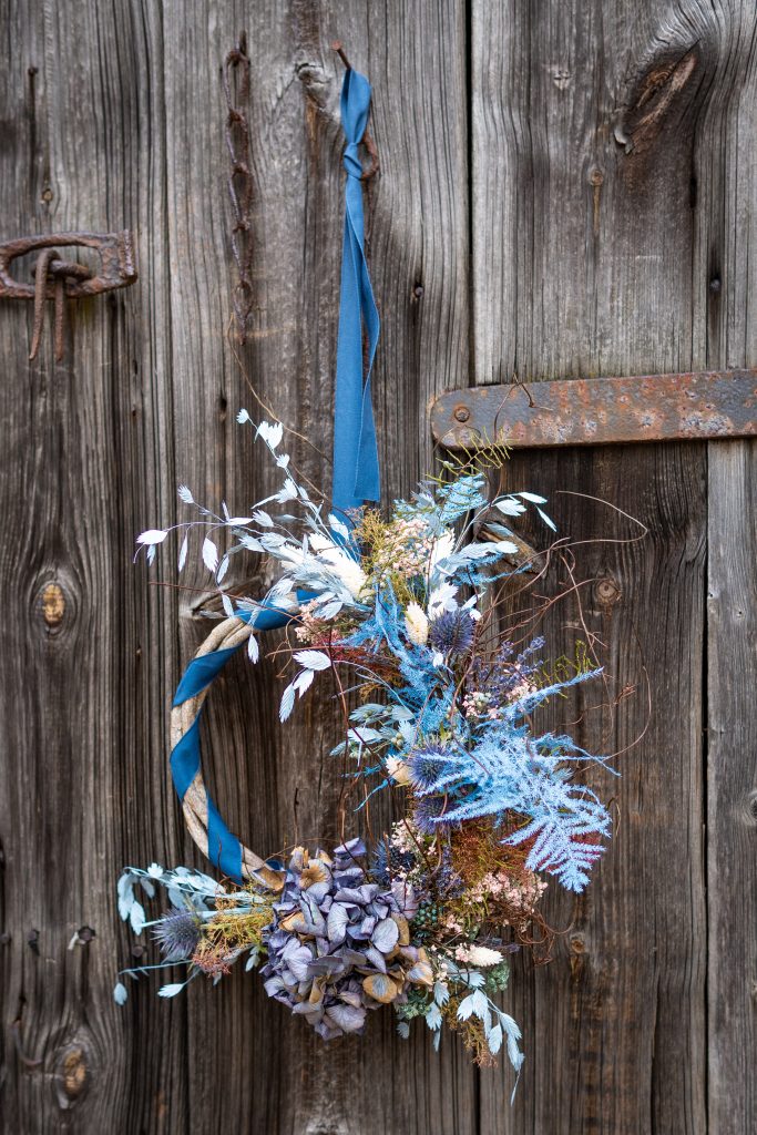 1. Dekorative Kr&auml;uter- und Blumengirlande an rustikaler Holzt&uuml;r f&uuml;r nachhaltiges Gedeihen.