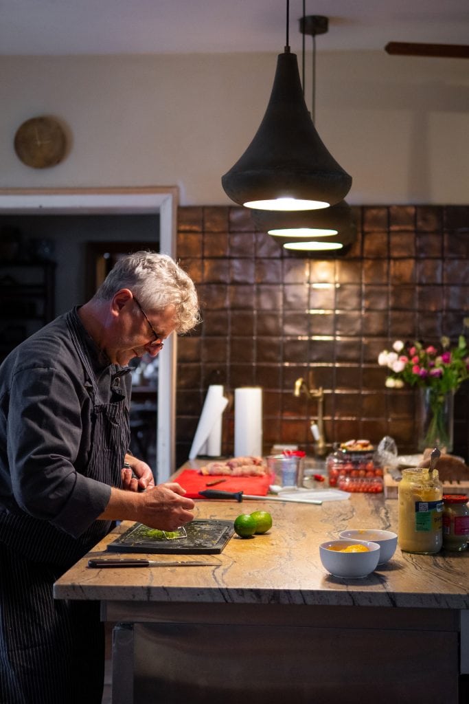 Frischer Koch beim Zubereiten in moderner, gem&uuml;tlicher K&uuml;che mit Fokus auf gesunde Ern&auml;hrung und Lebensmittelqualit&auml;t.