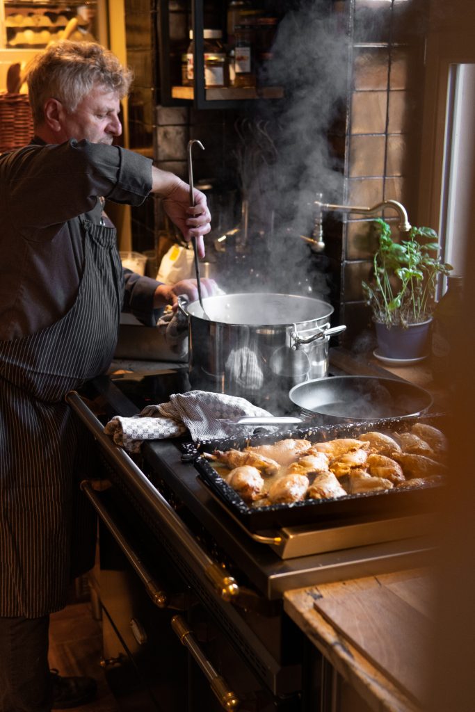 Knoblauchkoch in gemütlicher Küche, frische Kräuter im Topf, authentisches Kocherlebnis, nachhaltige Ernährung, biologisch.