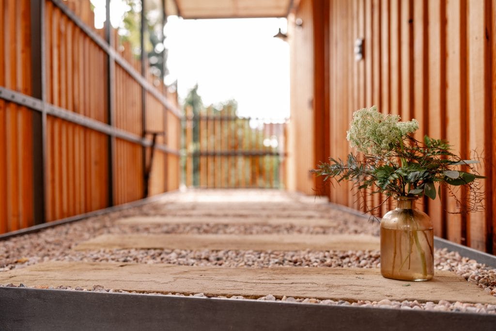 Naturnaher Gartenweg mit Holzplatten und Steinen, umgeben von Holzspalieren.