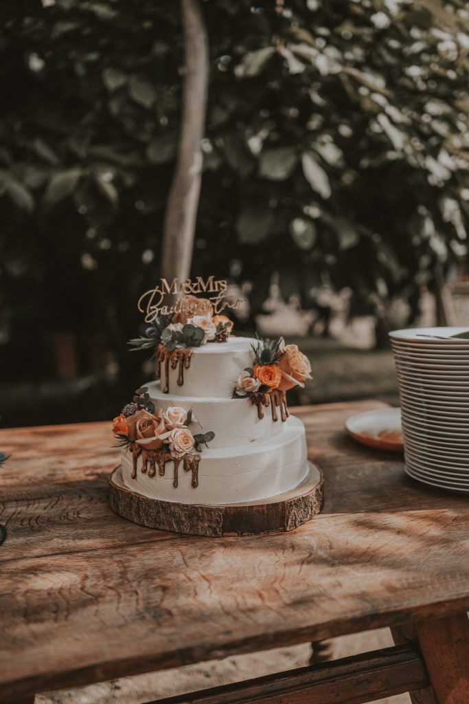 Hochzeitstorte mit Blumen und "Mr & Mrs" Schriftzug auf rustikalem Holztablett.