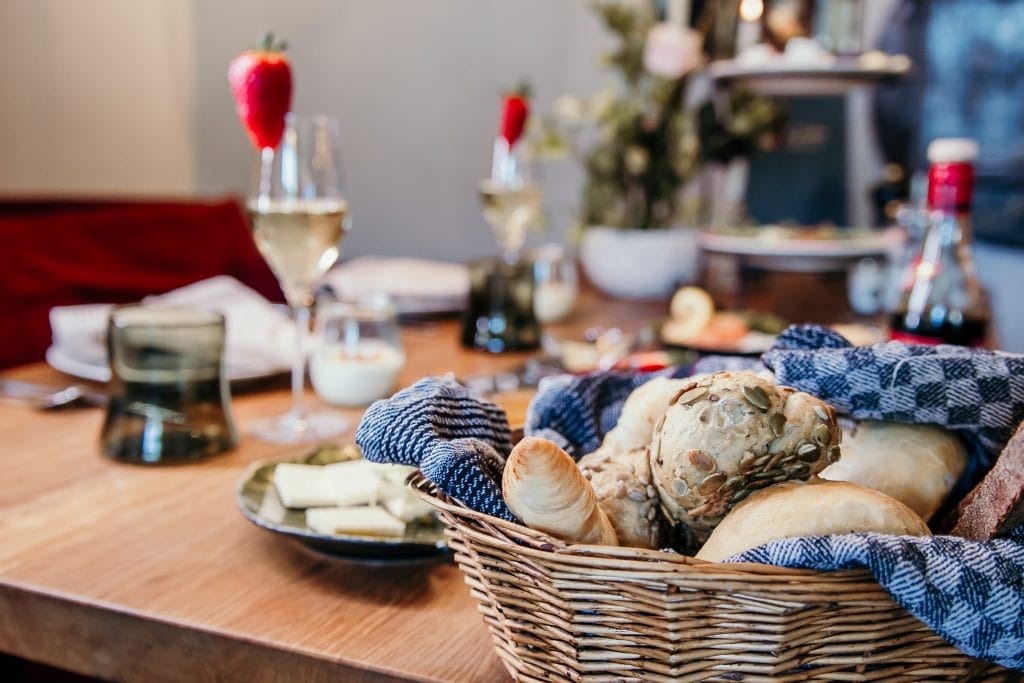 Frühstücksbrotkorb mit verschiedenen Brötchen und Kerzen auf gedecktem Tisch in gemütlicher Atmosphäre.