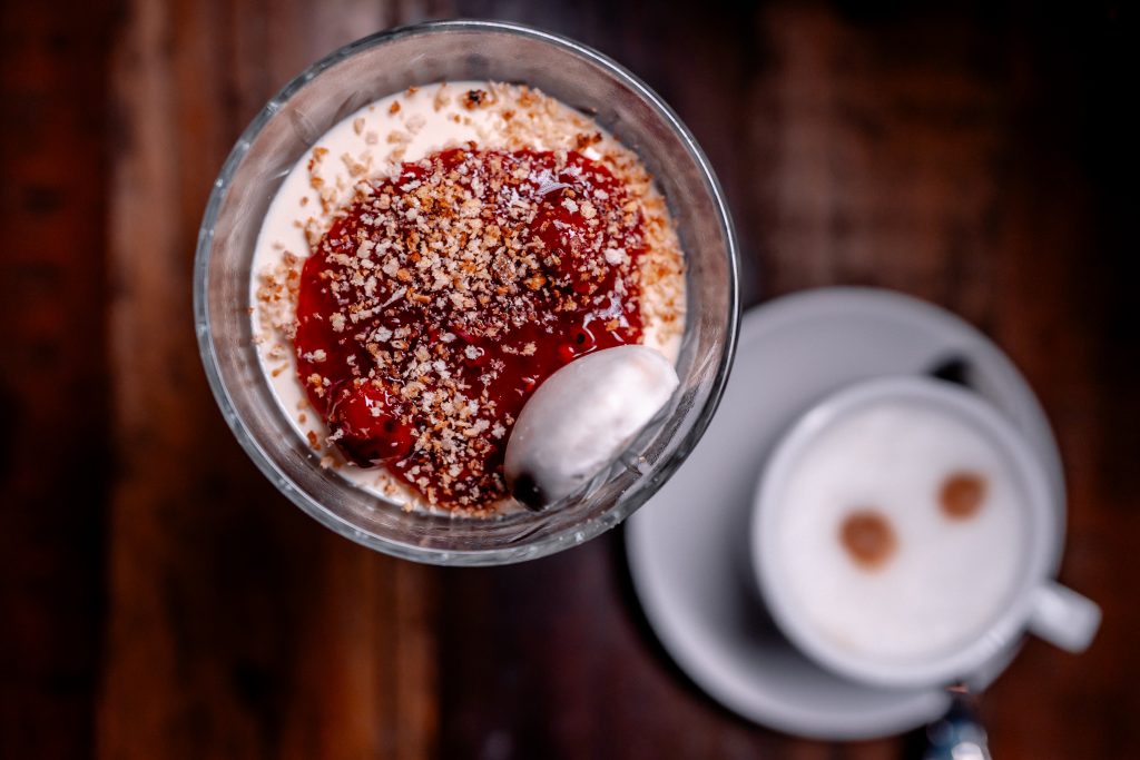 FrĂĽhstĂĽck mit Joghurt, Beeren und NĂĽssen auf einem Holztablett.