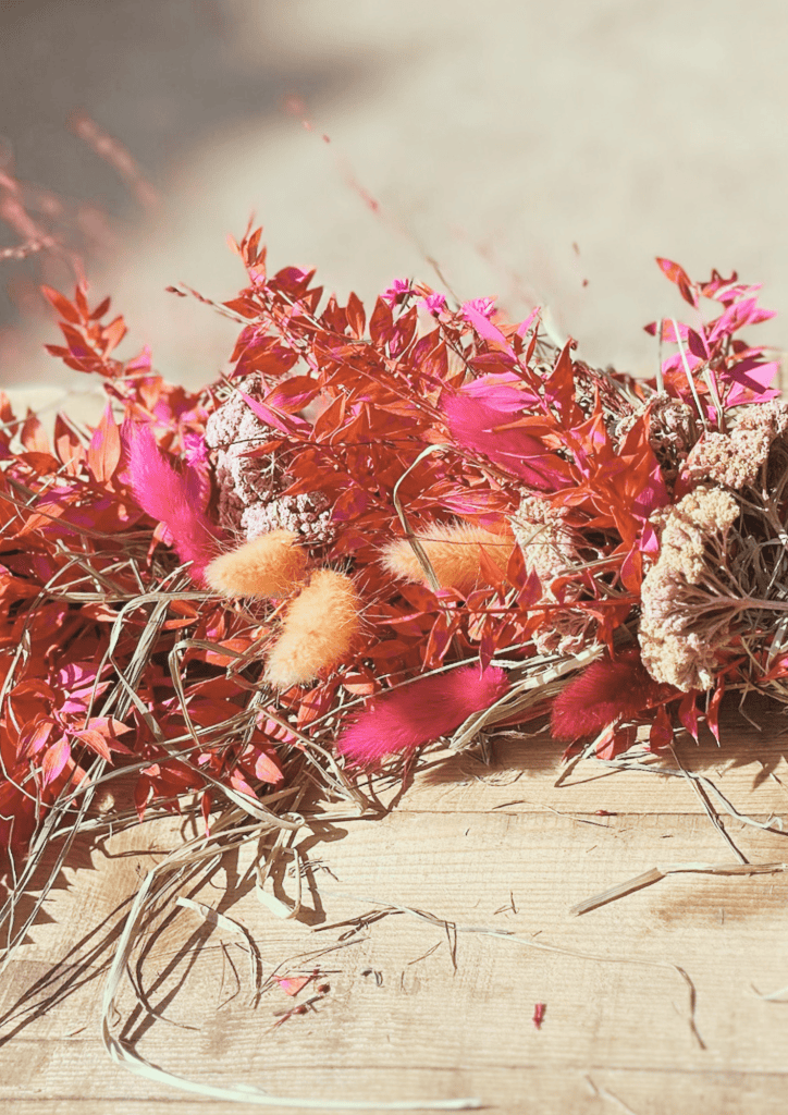 Farbenfroher Trockenblumenstrauß mit roten, pinken und beigen Akzenten auf Holzuntergrund.