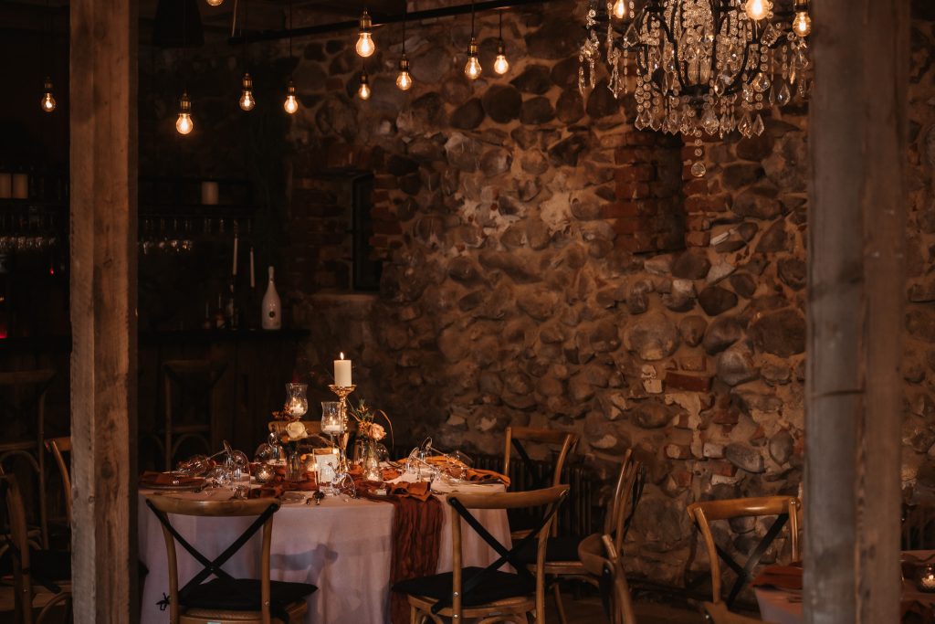 Gemütlicher festlicher Speisesaal mit Kerzen, Blumen und Kristallleuchter, rustikale Steinwände.