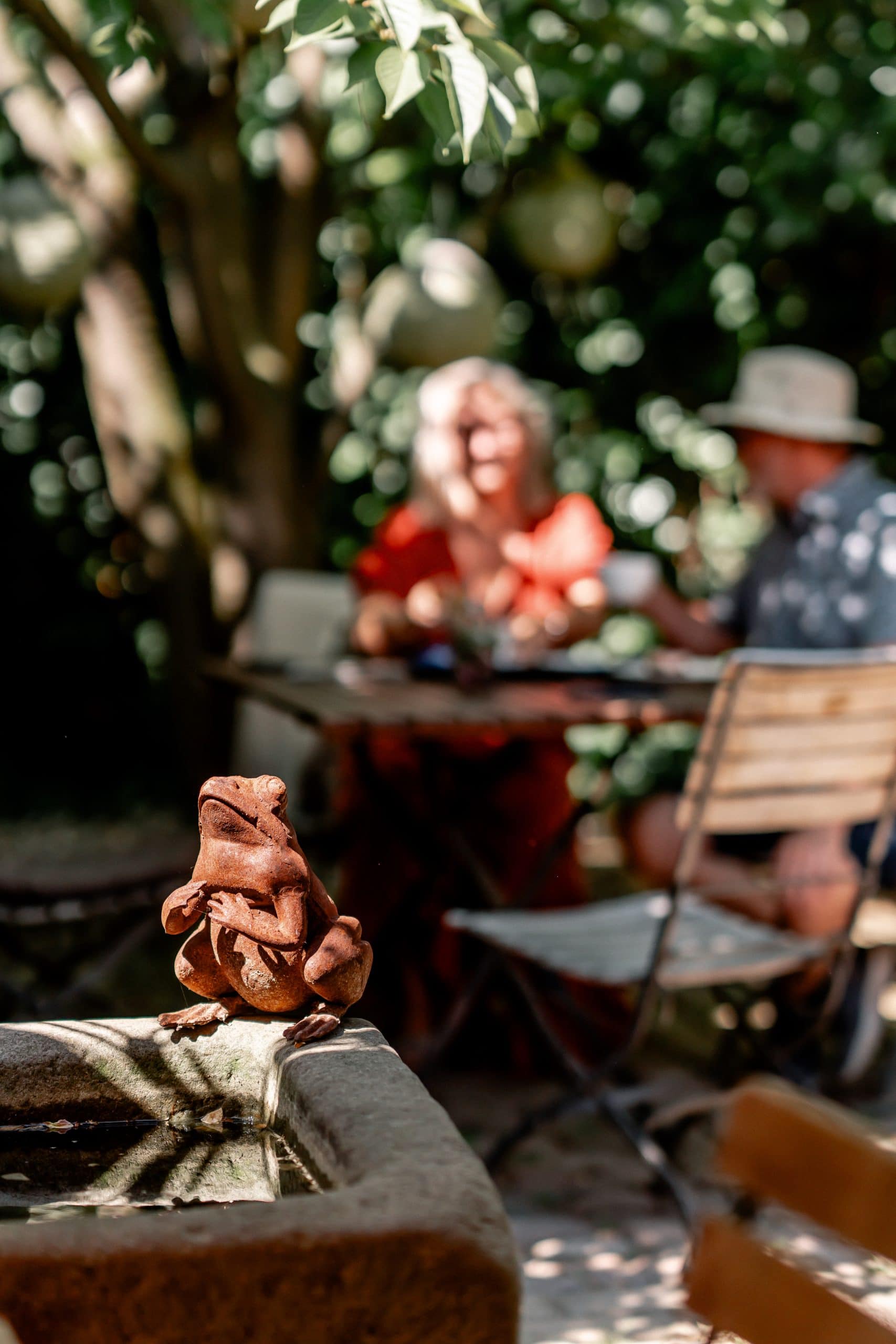 Fröschchen aus Terrakotta im Garten, entspannte Menschen im Schatten, Natur, Erholung, nachhaltiges Leben.