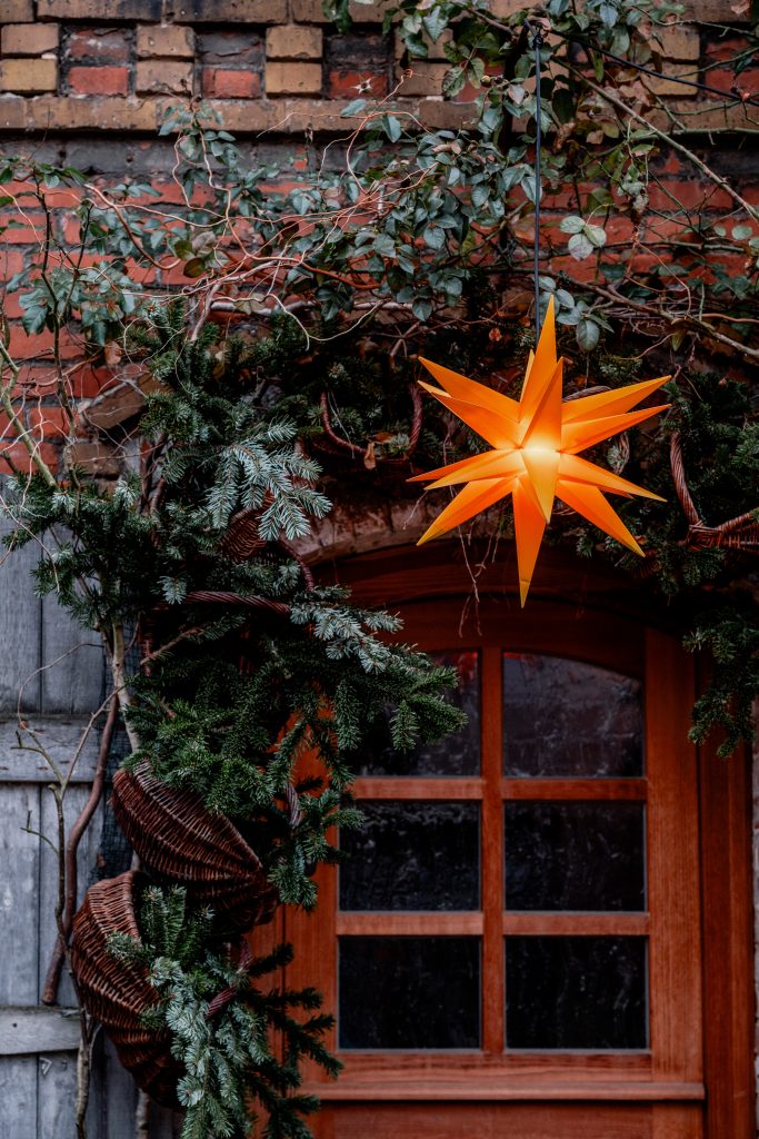 Hängende Weihnachtsstern-Laterne über einem Fenster mit Tannenzweigen und Efeu, festliche Dekoration.