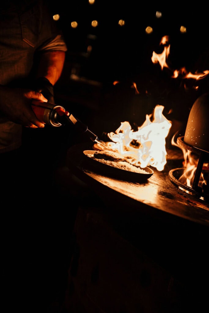 Person beim Flambieren einer Pizza bei einer Küchenparty im Waldrausch.