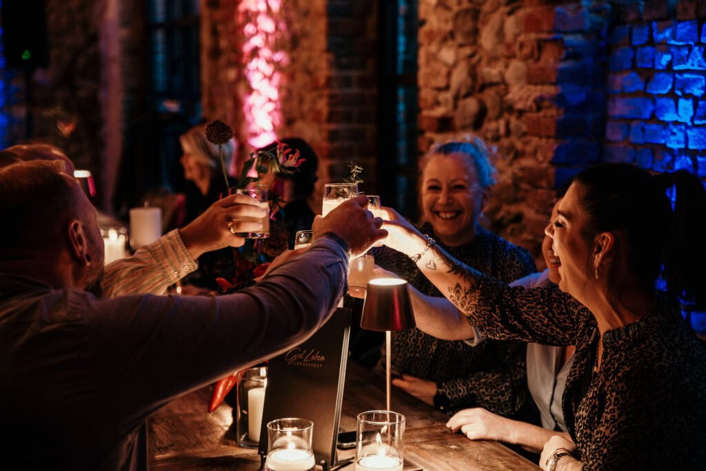 Menschen bei einer Küchenparty in einem rustikalen Ambiente mit Kerzen und Getränken.