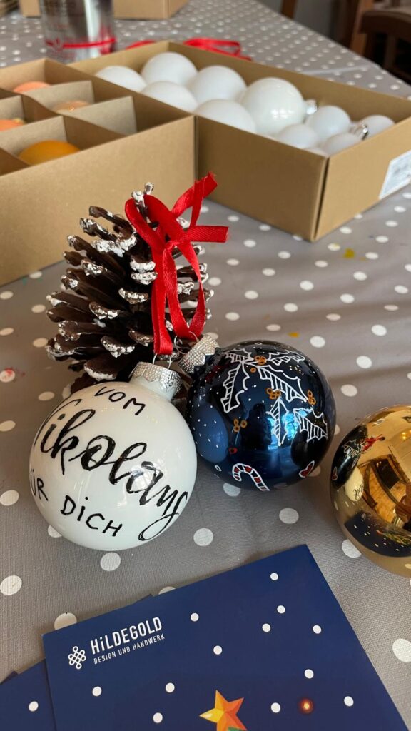 Weihnachtliche Kalligrafie mit dekorativen Weihnachtskugeln und Geschenkboxen.