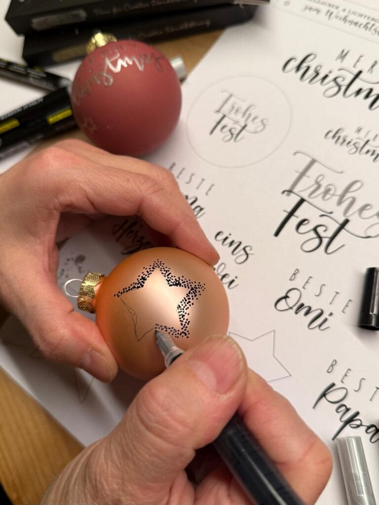 Weihnachtliche Kalligrafie auf Christbaumkugeln und Papier.