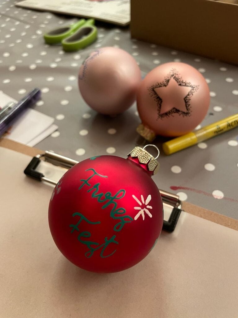 Weihnachtliche Dekoration mit Kugeln und Kalligrafie auf einem Tisch.