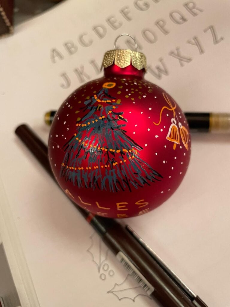 Rote Weihnachtskugel mit Tannenbaum und goldenen Akzenten auf Papier.