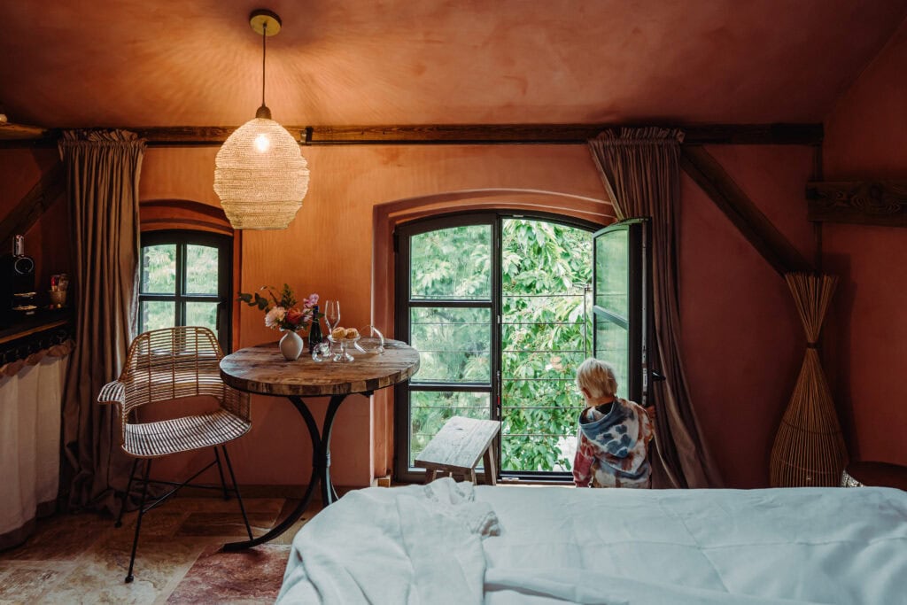 Gemütliches Schlafzimmer mit Blick auf grüne Natur durch offene Fenster.