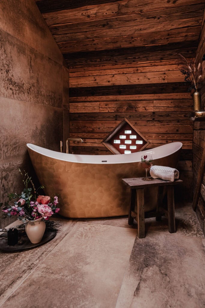 Elegante Badewanne im rustikalen Badezimmer mit Holzdecke und Blumen.