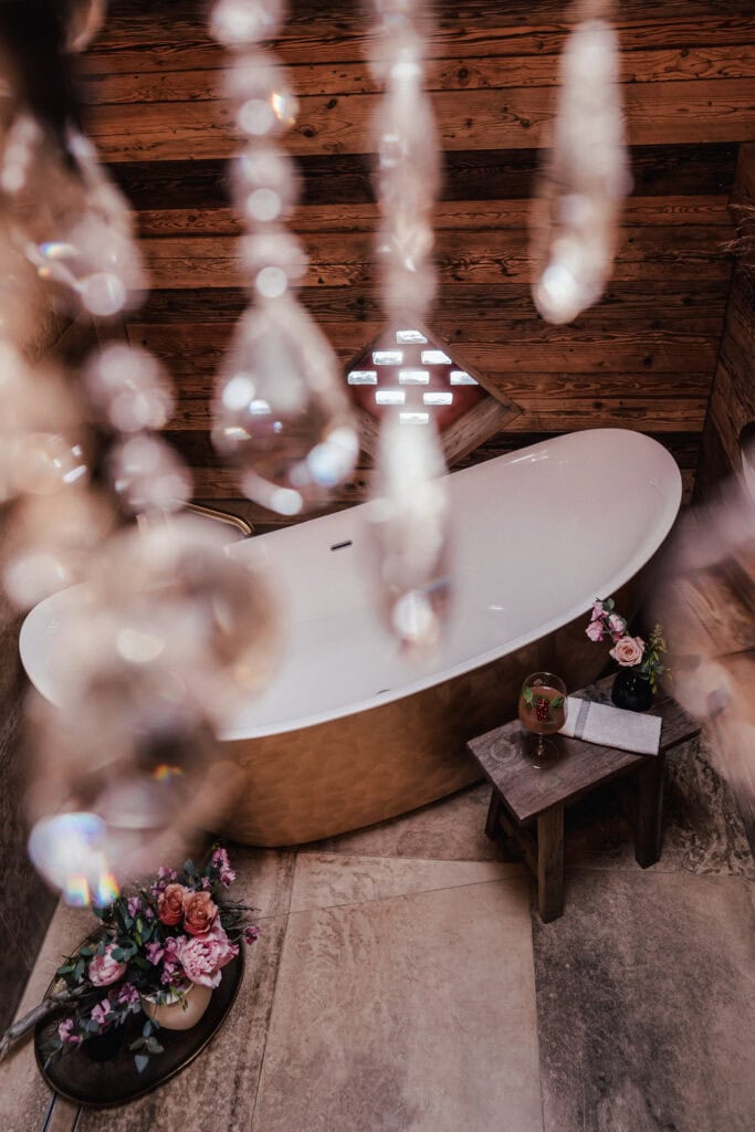 Elegante Badewanne im rustikalen Badezimmer mit Blumen und Kristallleuchter.