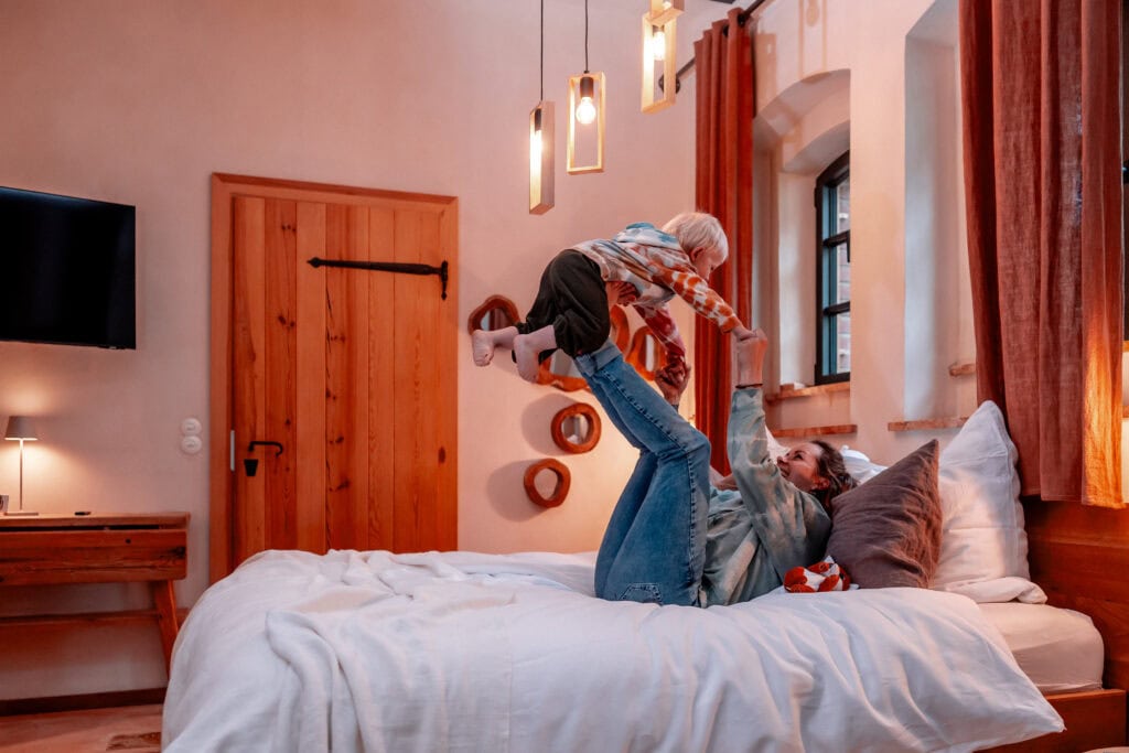 Mutter spielt mit Kind auf einem Bett in einem gemütlichen Schlafzimmer.