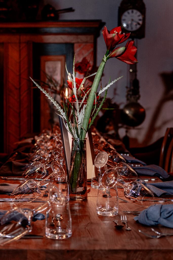 Eleganter gedeckter Tisch mit roter Amaryllis und Gläsern für ein festliches Essen.